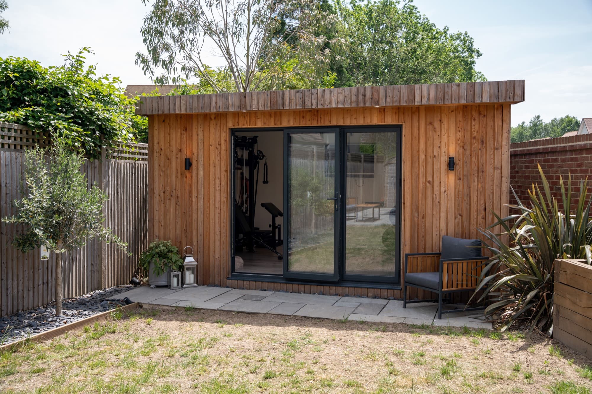 Timber clad garden gym with wide bifold doors, seen across the lawn